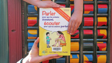 Un livre est tenu par le bas par une main d'adulte et par le haut par deux mains d'enfants