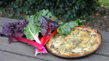 Une tarte aux blettes ainsi qu'un bouquet de blettes sont posés sur une table en bois